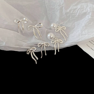 Boucles d'oreilles nœuds argentées avec perles blanches sur fond minimaliste chic