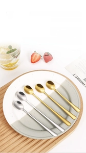 Close-up of polished gold and silver stainless steel round spoons on a ceramic plate
