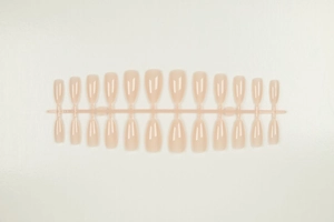 Detailed view of almond shaped nude pink press-on nail tips on professional salon display