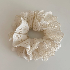 Détail macro d'un chouchou en dentelle crème avec broderie florale et texture ajourée