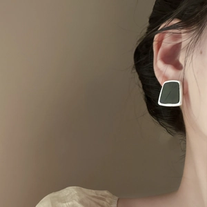 Detail of geometric resin earring with silver metal edge worn on model's ear
