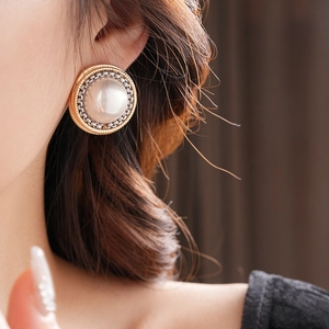 Gros plan d'une boucle d'oreille perle vintage avec bordure dorée et argentée sur modèle
