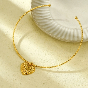 Close-up of golden heart pendant necklace with quilted texture and ball-end choker band