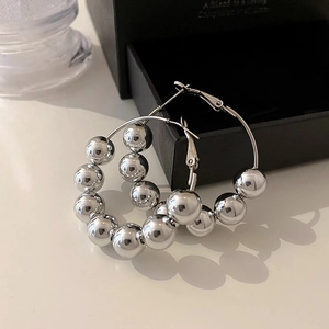 Detail view of silver bead hoop earrings with polished metallic spheres on a white desk