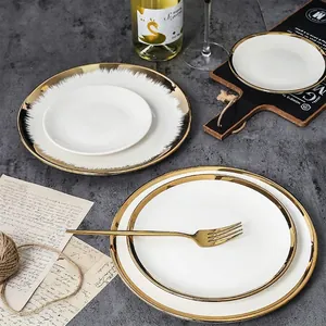 Nordic white ceramic plates with wide gold rims and cutlery on a dark stone table
