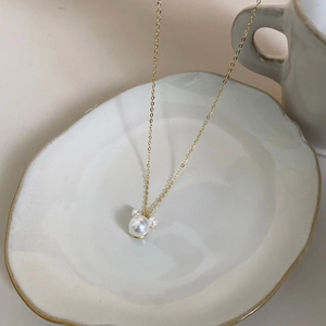 Detailed shot of a gold pearl necklace with Mickey-shaped pendant on a ceramic tray