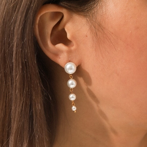 Close-up of elegant 18k gold earrings with four graduated white pearls on a female model