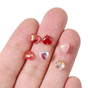 Mini perles en verre en forme de cœur pour bijoux DIY posées sur le bout du doigt