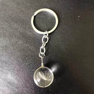 Close-up of a clear glass sphere keychain featuring real dandelion seeds inside