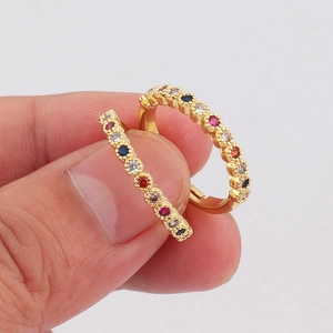Pendientes de aro dorados con circonitas de colores sujetos entre los dedos sobre fondo neutro