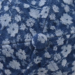 Macro view of blue denim baseball cap crown showing floral texture and fabric button