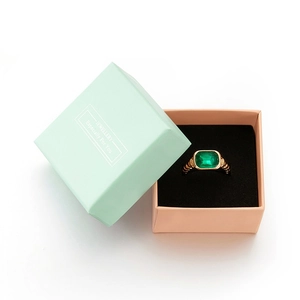 Detail of a gold ring with green gemstone next to a light green jewelry gift box