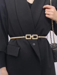 Close-up of interlocking square buckle on a gold elastic metal waist chain over a blazer