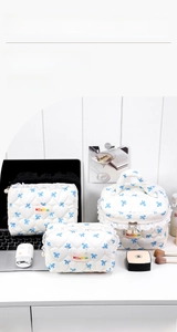 Detailed set of three quilted white makeup bags with blue bow prints and lace zipper trim