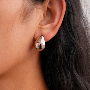 Close-up of a drop-shaped gold earring with a mirror finish on a model side profile
