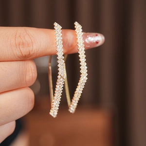Dettaglio di orecchini a rombo dorati con cristalli brillanti e un design curvo unico e raffinato