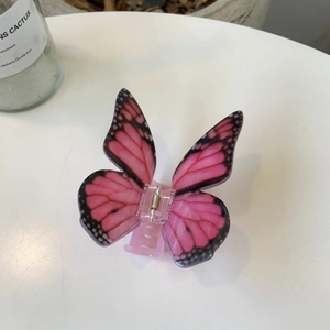 Pink butterfly acrylic hair claw clip with black spotted wings on a white surface