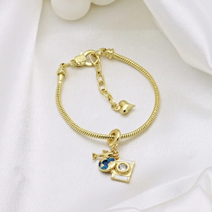 Detail of gold camera charm with blue enamel on a snake chain bracelet with heart clasp