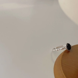 Minimalist silver ring with black oval gemstone on a smooth dark wooden base