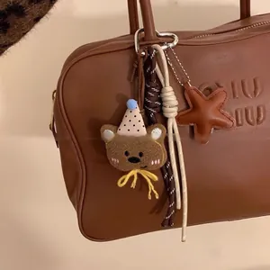 Dettaglio di una borsa in pelle marrone con ciondolo a forma di orsetto e stella in pelle