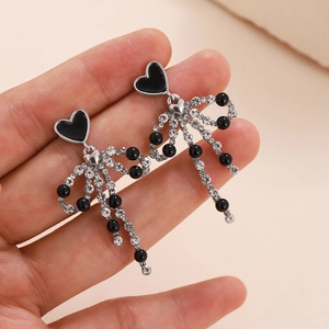 Silver drop earrings with black heart studs and crystal bow tassels held by hand
