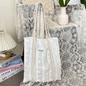 Vue détaillée des broderies florales blanches et de la texture de ce sac en dentelle