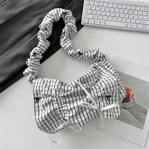 Detailed view of checkered pleated handbag with black bow embroidery on a desk