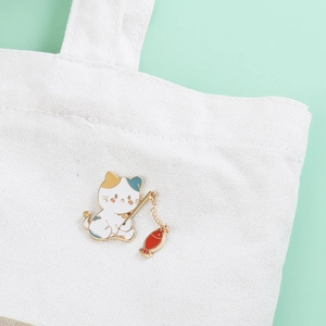 Macro detail of cat fishing enamel pin with gold chain on canvas bag for bags and hats