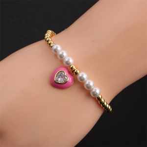 Gold beaded bracelet with white pearls and pink heart zircon pendant on a wrist