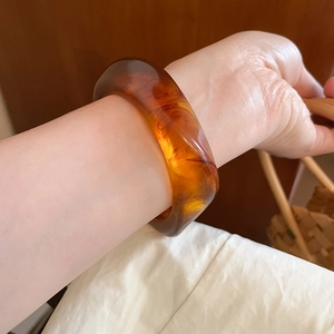 Detail of wide amber resin bangle featuring classic tortoiseshell patterns worn on wrist