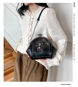 Side view of black rivet shell bag with bear charm and tassel on a stylish model