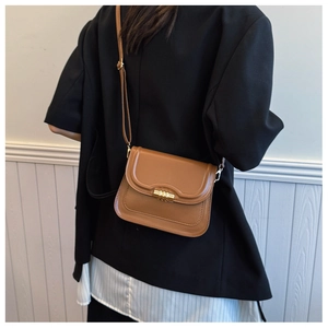 Détail d'un sac besace marron avec fermoir doré porté sur une veste de blazer noire