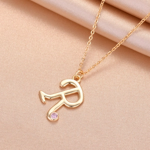Detail of gold letter R pendant necklace with a sparkling pink gemstone on silk fabric