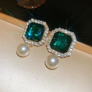 Macro detail of emerald cut green gemstone earrings with pavé diamonds and white pearls