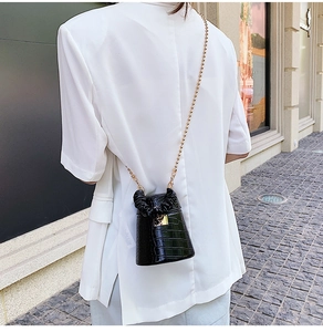 Detail of black crocodile texture bucket bag with elegant gold chain strap on a model