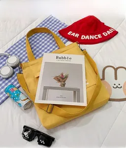 Flat lay of a yellow canvas tote bag with shoulder straps and red bucket hat on a bed