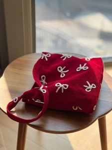 Detail of red corduroy shoulder bag with white embroidered bows on a wooden stool