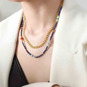 Detail of layered gold leaf chain and blue beaded necklace worn on a model