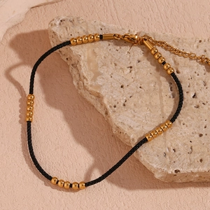 Close-up of 18K gold plated steel beads on black cord anklet resting on natural stone