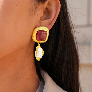 Detail view of irregular pearl and red resin earrings with hammered gold texture on model
