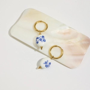 Dettaglio degli orecchini in porcellana con fiori blu e cerchi dorati in titanio 18K