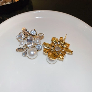 Detailed view of pearl and crystal drop earrings with silver needle on white plate