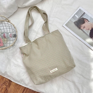 Flat lay of pink and green checkered canvas tote bag with leather tag on white linen
