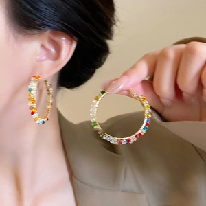 Detail of gold large hoop earrings with colorful crystals worn by a female model