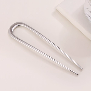 Minimalist silver U-shaped metal hair pin on light beige background with book decoration