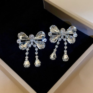 Detail of silver bow earrings with sparkling crystals and long tassels on black velvet