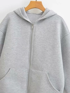 Detail of grey zip-up hoodie featuring drawstring hood, large pockets and knit texture