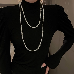 Detail of layered white pearl necklace on black turtleneck sweater showing elegant luster