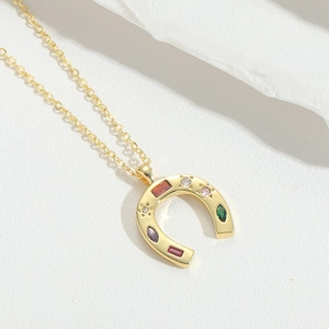 Close-up of golden horseshoe pendant with colorful inlaid zircons on a delicate chain