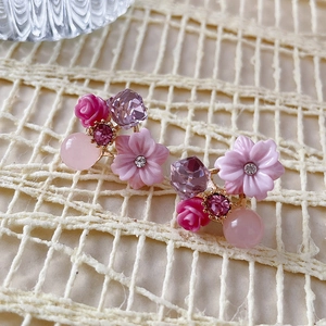 Macro shot of floral earrings with pink opal and purple crystals on beige woven background
